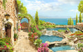 Mediterranean courtyard wallpaper | Sea view garden style mural with stone pathway, archway, lush flowers, terraced pool, and  coastal blue sea view