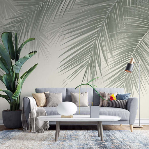 Palm leaf wallpaper mural | Fresh decorative wall in living room and bedroom in a modern lounge with a gray sofa, tropical plants, and sunlit ambience