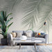Palm leaf wallpaper mural | Fresh decorative wall in living room and bedroom in a modern lounge with a gray sofa, tropical plants, and sunlit ambience